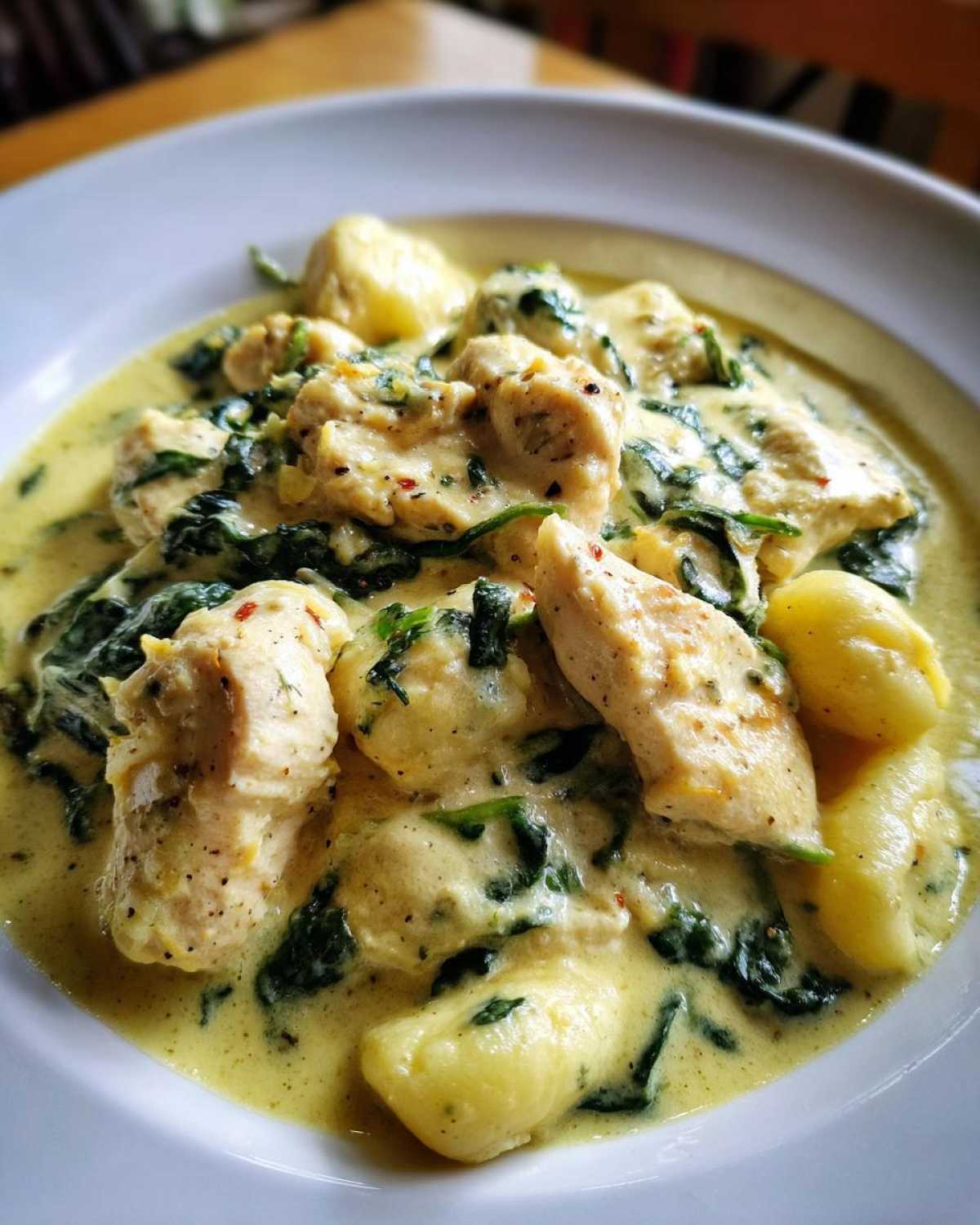 Close-up of Creamy Chicken Gnocchi with Garlic Sauce, featuring tender chicken pieces and spinach in a rich yellow sauce.