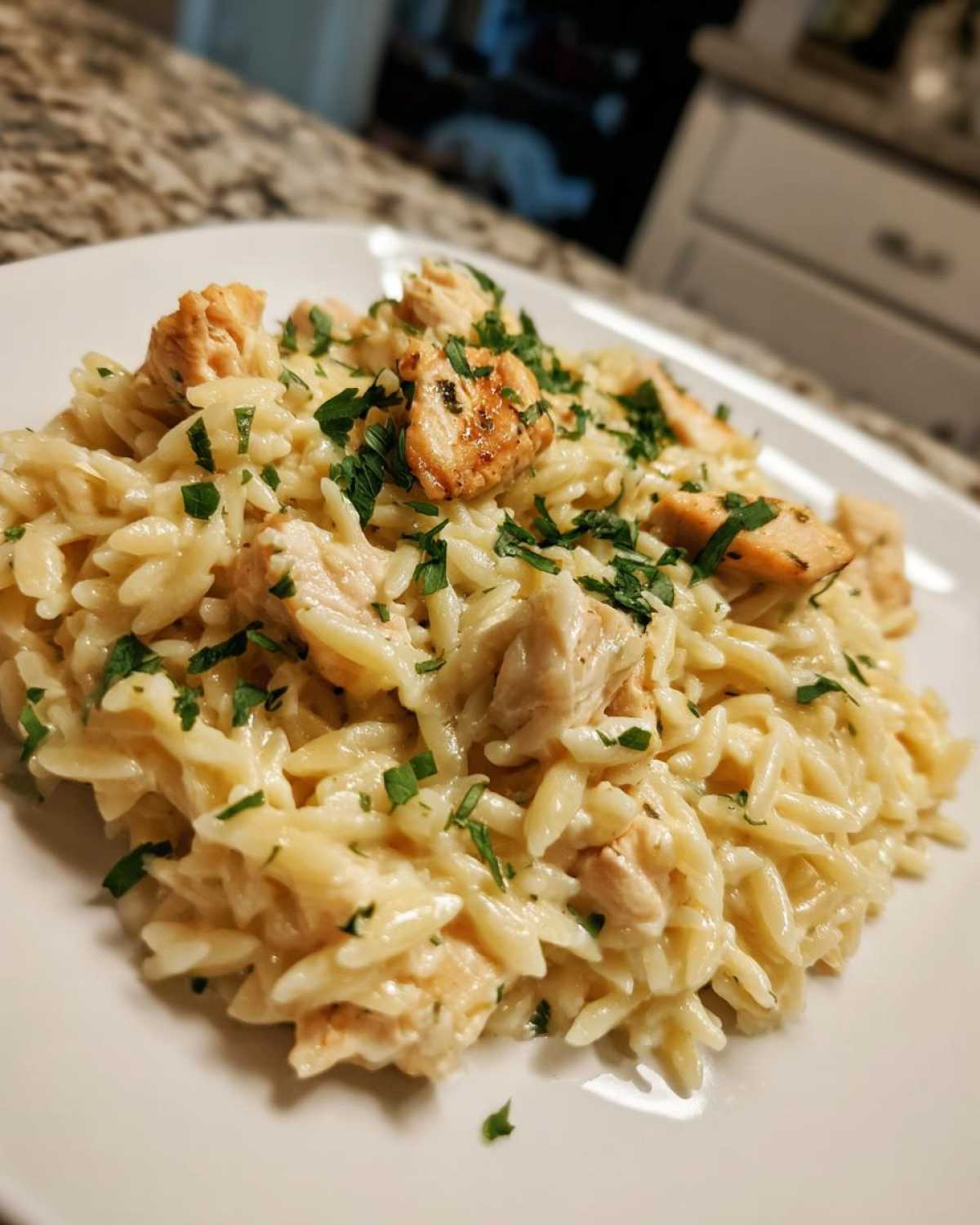 A close-up of a serving of Creamy Garlic Parmesan Orzo with Chicken, topped with fresh parsley.
