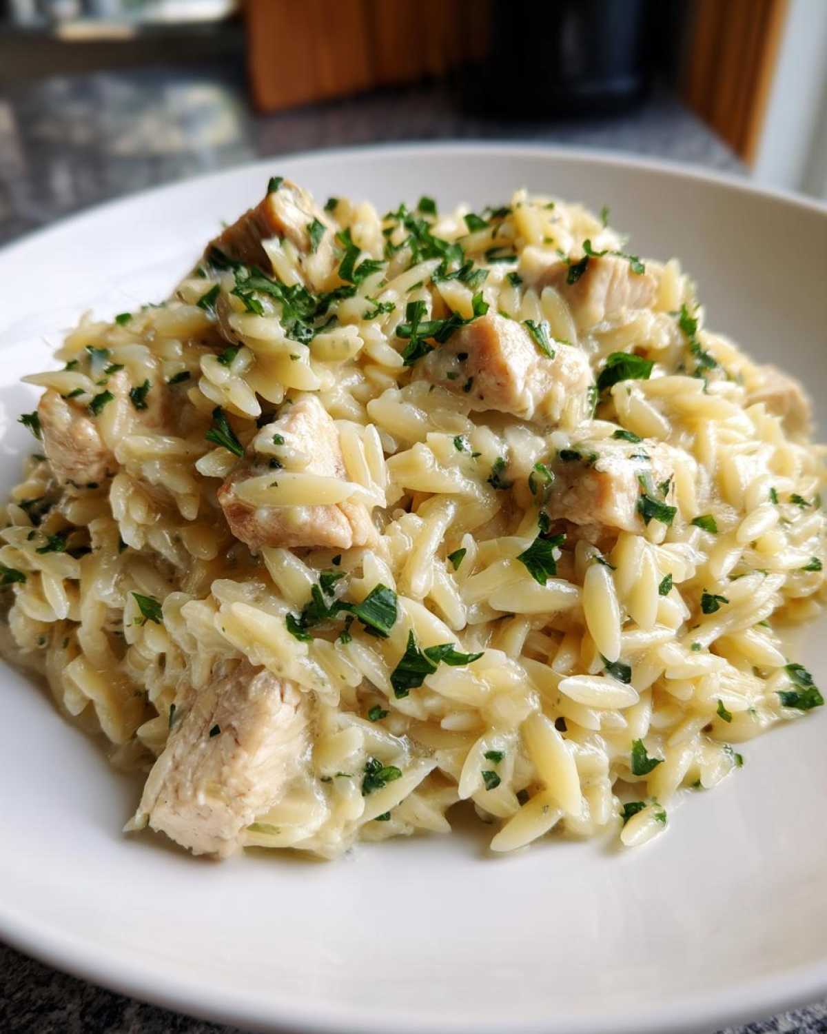 A close-up of a white bowl filled with Creamy Garlic Parmesan Orzo with Chicken, topped with fresh parsley.
