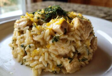 A mound of creamy Lemon Chicken Orzo with chunks of chicken, topped with lemon zest and fresh dill.