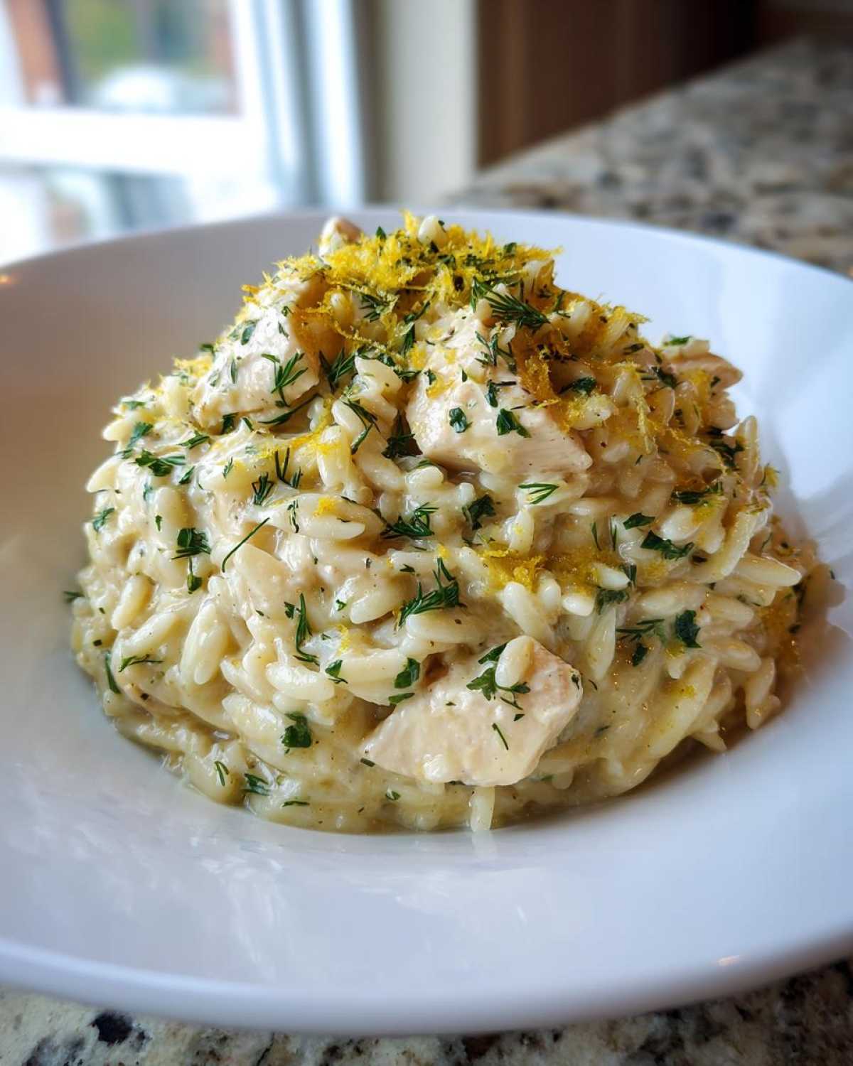 A bowl of Creamy Lemon Chicken Orzo topped generously with fresh herbs and bright yellow lemon zest.