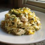 A close-up of a serving of Creamy Lemon Chicken Orzo, topped with fresh herbs and lemon zest.