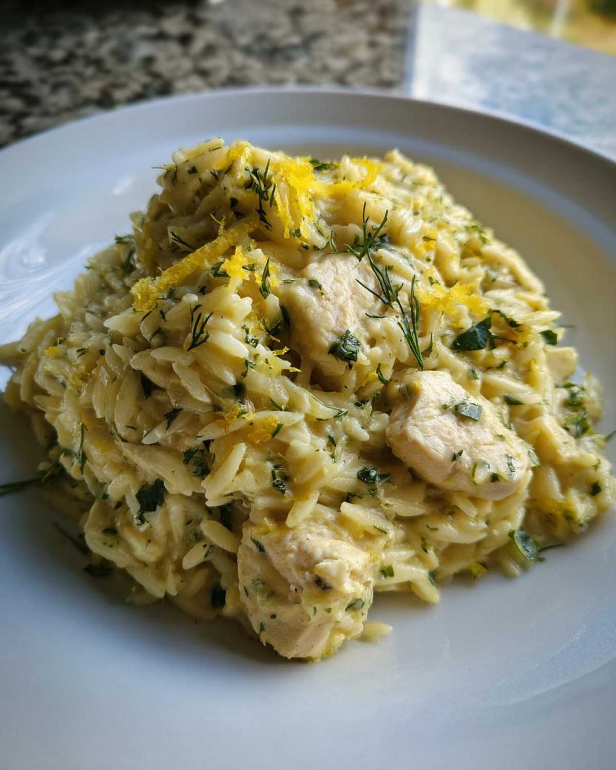 A serving of Creamy Lemon Chicken Orzo topped with fresh lemon zest and dill on a white plate.
