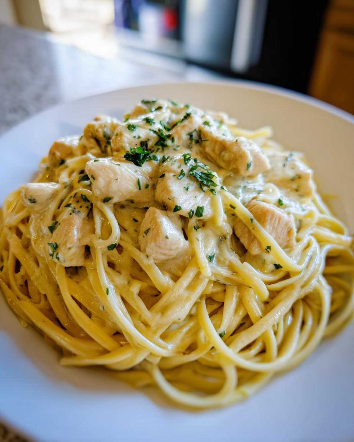Close-up of a bowl of Creamy Lemon Chicken Pasta, featuring linguine tossed in a rich sauce with diced chicken and fresh parsley.