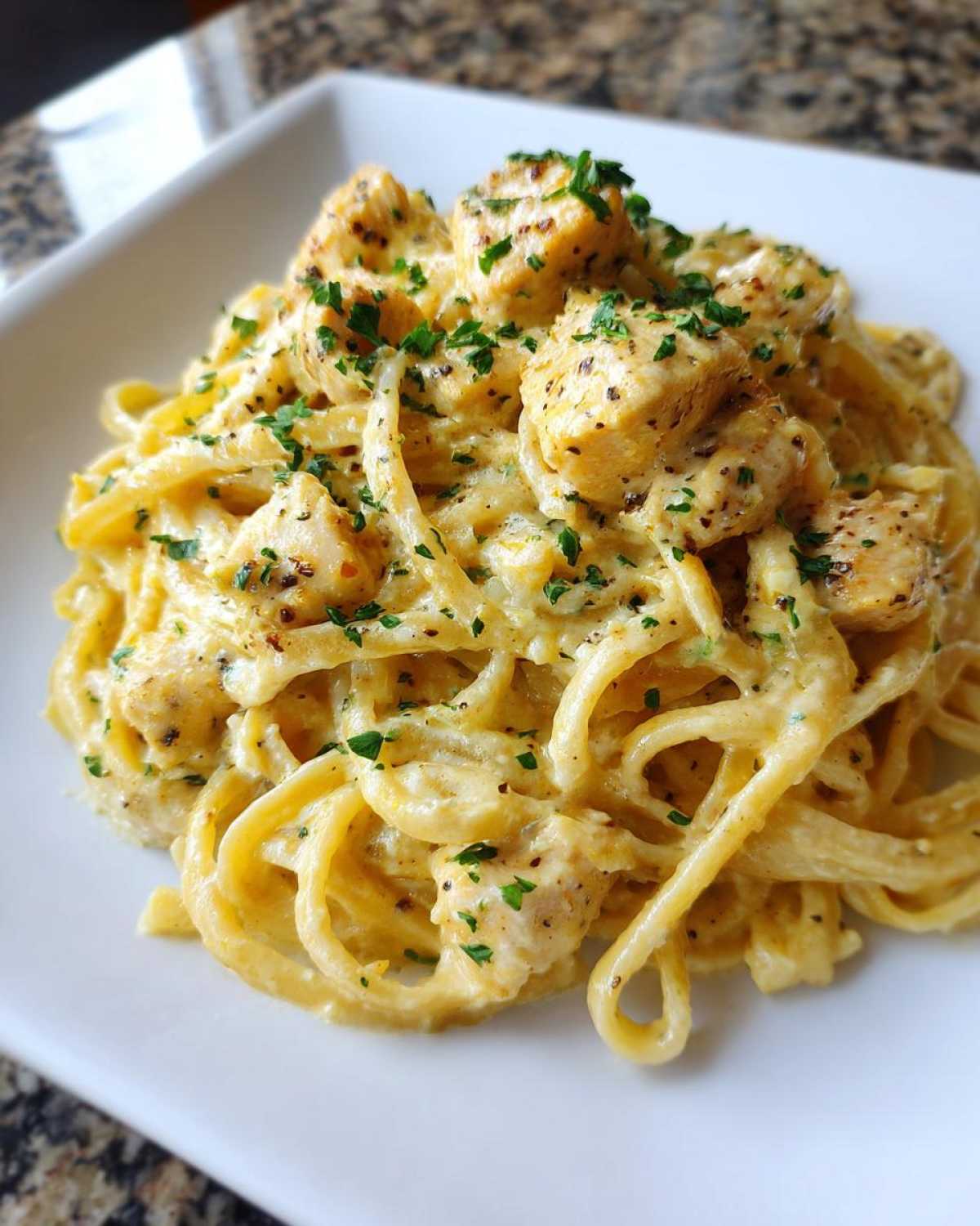 Close-up of a white square plate holding a serving of Creamy Lemon Chicken Pasta Fresh and Light, topped with parsley.