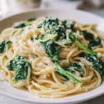 A close-up of Creamy Lemon Ricotta Pasta with Spinach tossed in a white bowl, topped with grated cheese.