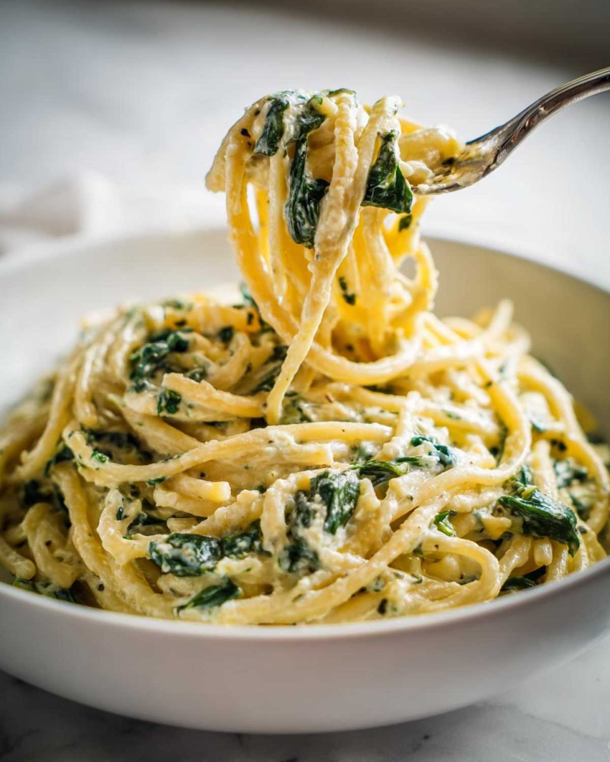 A fork lifting a twirl of Creamy Lemon Ricotta Pasta with Spinach from a white bowl.