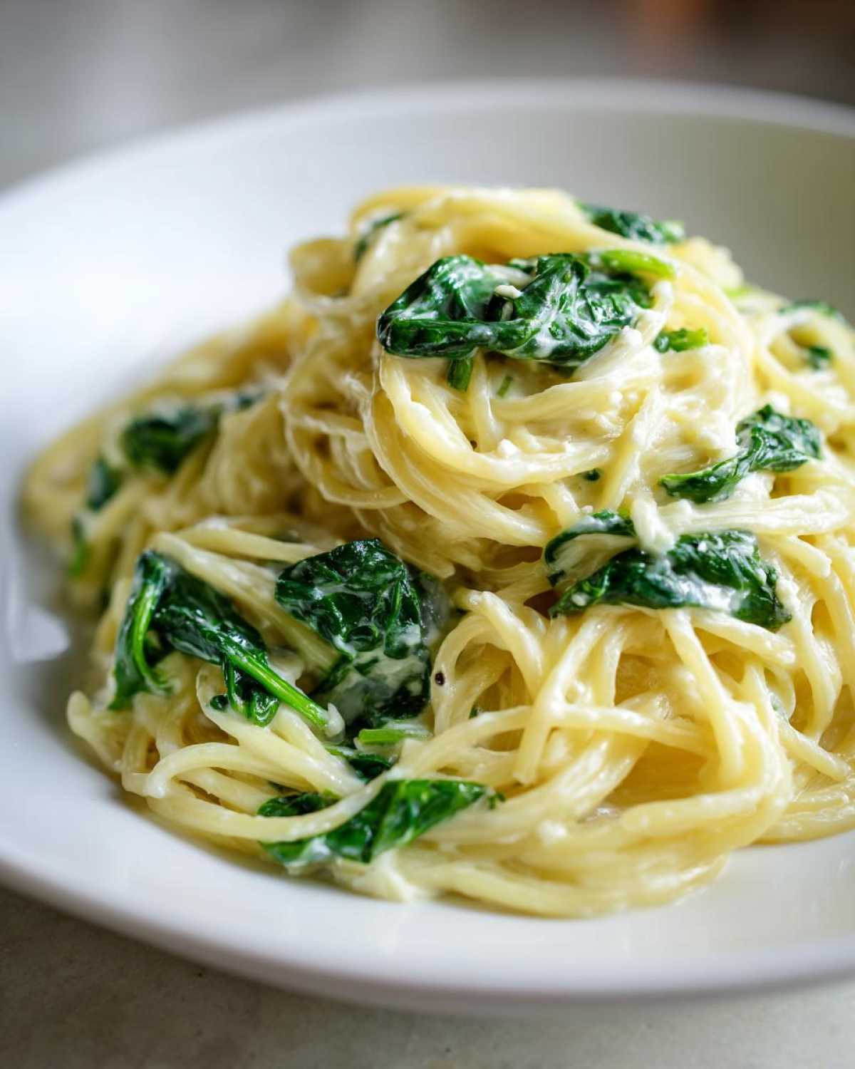 Close-up of creamy lemon ricotta pasta with spinach tossed with spaghetti noodles in a white bowl.