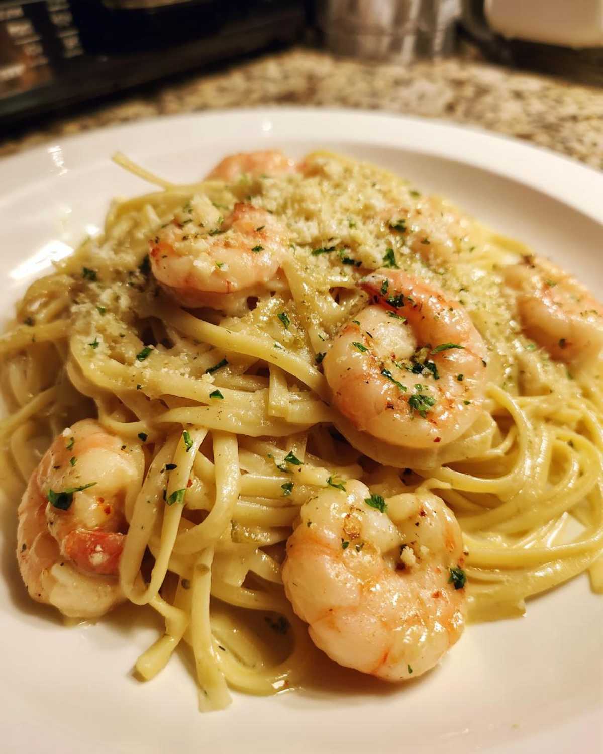 Close-up of a serving of Creamy Lemon Shrimp Pasta tossed in a rich sauce, topped with pink shrimp, grated Parmesan, and fresh parsley.