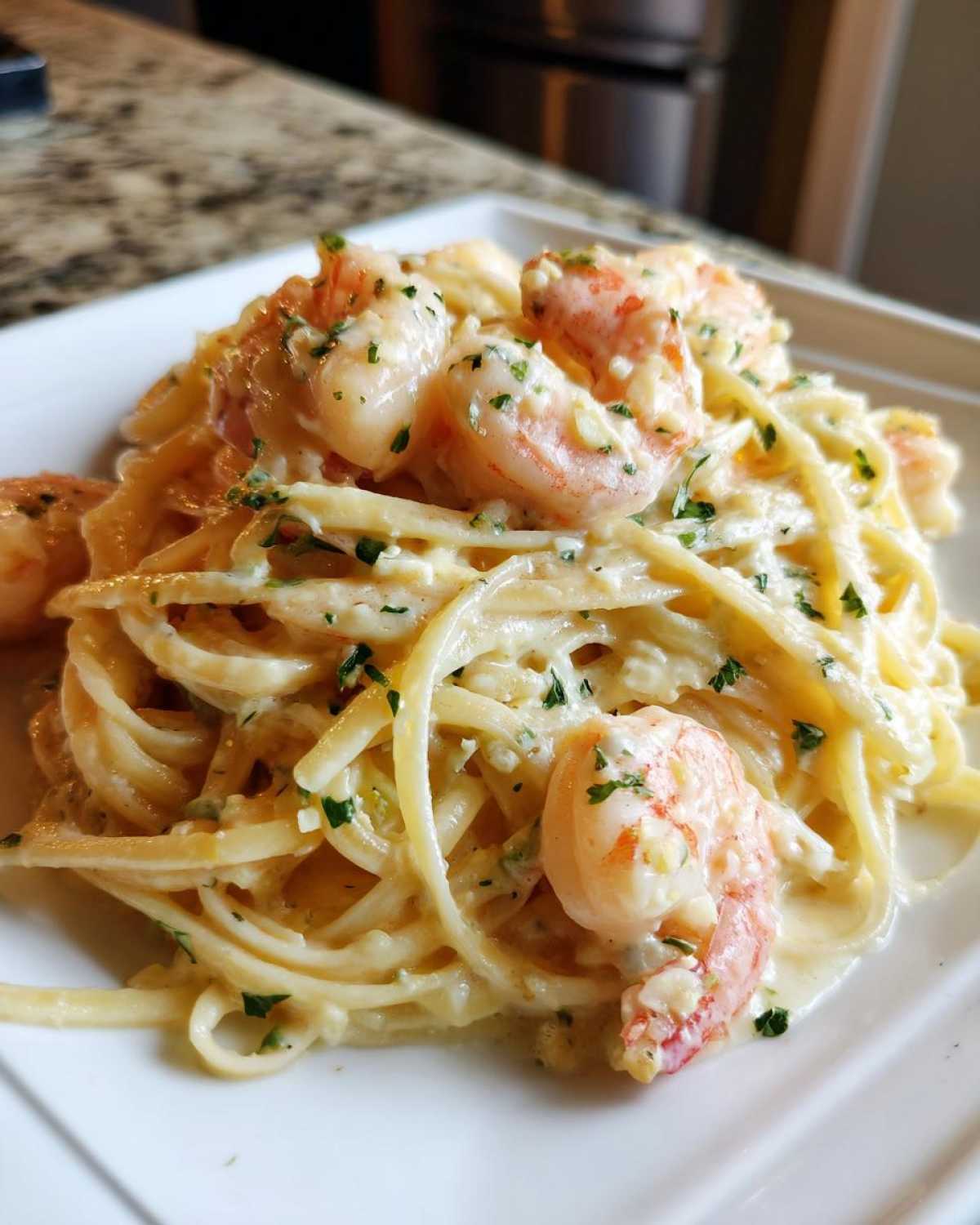 A close-up of Creamy Lemon Shrimp Pasta featuring linguine coated in a rich sauce and topped with pink shrimp and parsley.