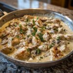 Close-up of seared chicken pieces and sliced mushrooms coated in a rich sauce in the Creamy Mushroom Alfredo Chicken Skillet.