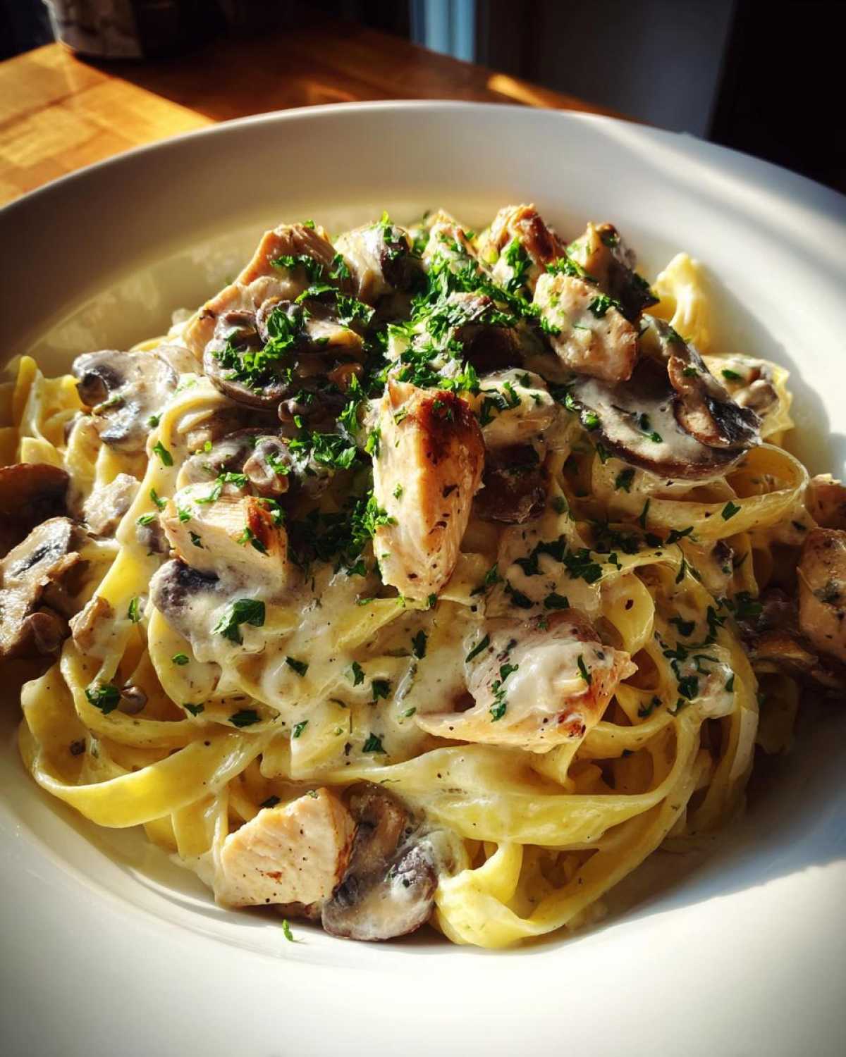 Close-up of a bowl of Creamy Mushroom Chicken Alfredo Pasta with fettuccine noodles and fresh parsley.