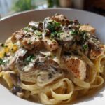 A close-up of a bowl of Creamy Mushroom Chicken Alfredo Pasta featuring fettuccine, seared chicken pieces, and sliced mushrooms in a rich sauce.