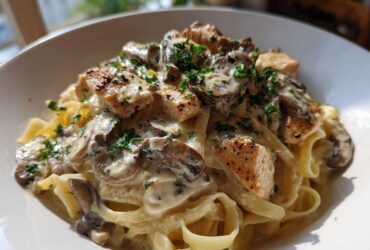 A close-up of a bowl of Creamy Mushroom Chicken Alfredo Pasta featuring fettuccine, seared chicken pieces, and sliced mushrooms in a rich sauce.