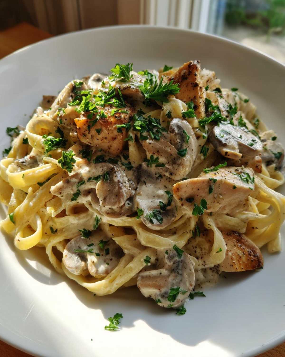 A close-up of a white bowl filled with Creamy Mushroom Chicken Alfredo Pasta, topped with fresh parsley.