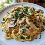 A close-up of a plate piled high with Creamy Mushroom Chicken Alfredo Pasta, topped with fresh parsley.
