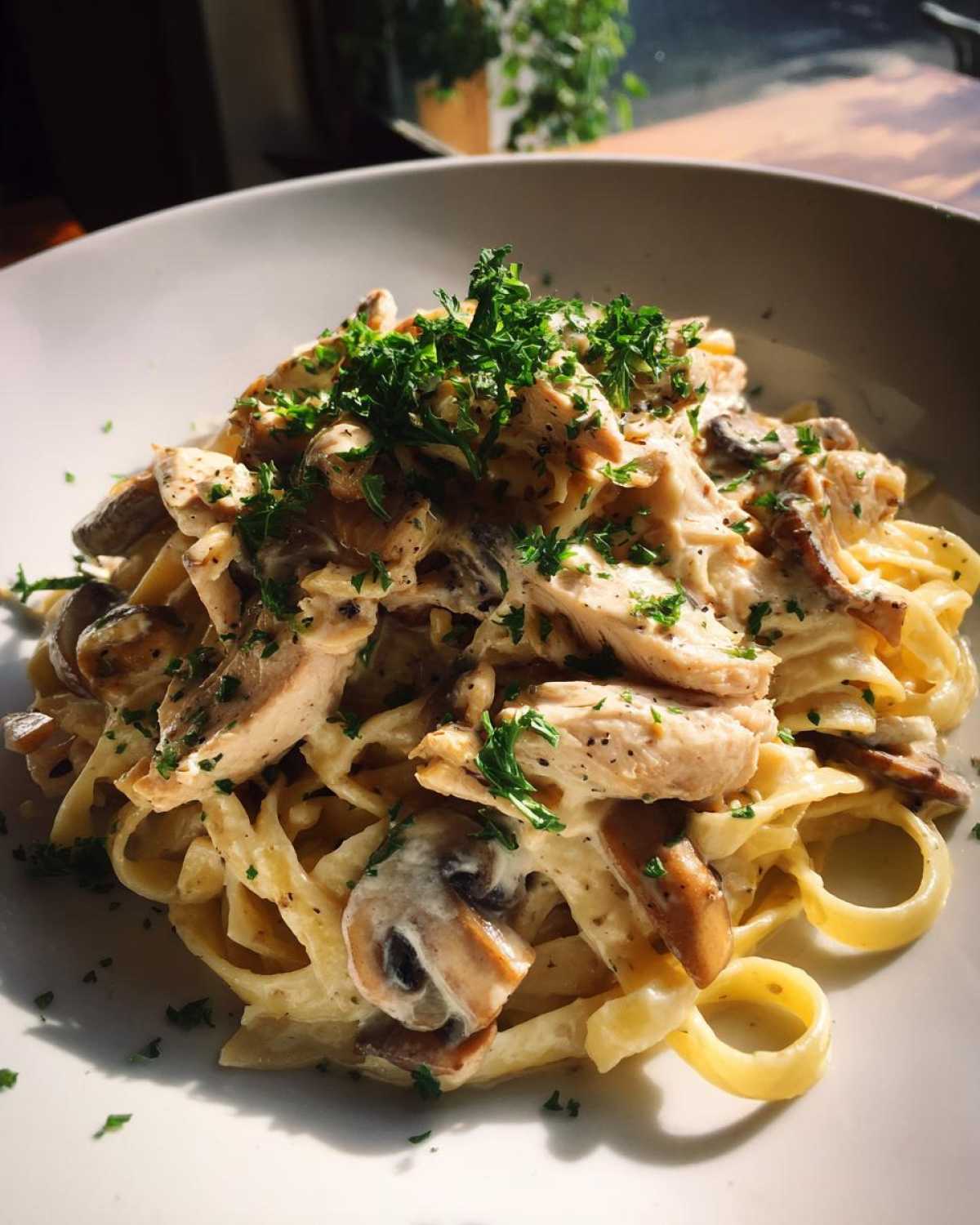 Close-up of a bowl of Creamy Mushroom Chicken Alfredo Pasta topped with fresh parsley.