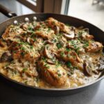 Close-up of tender chicken pieces and sliced mushrooms in a rich, creamy sauce, garnished with parsley, ready to serve from the skillet.