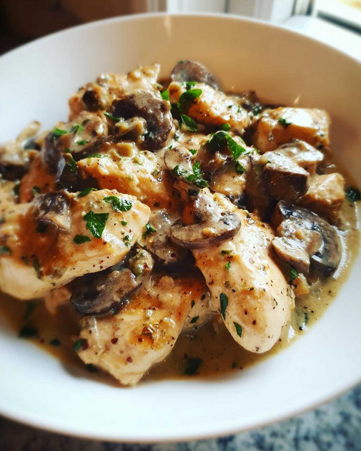 Close-up of tender chicken pieces smothered in a rich sauce with sliced mushrooms, garnished with parsley.