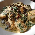 Close-up of chicken breasts smothered in a creamy mushroom and spinach sauce in a white bowl.