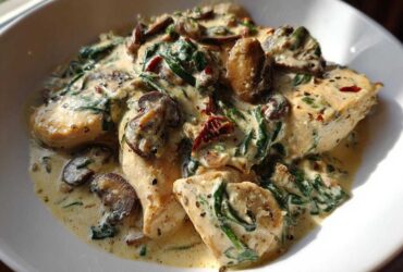 Close-up of chicken breasts smothered in a creamy mushroom and spinach sauce in a white bowl.
