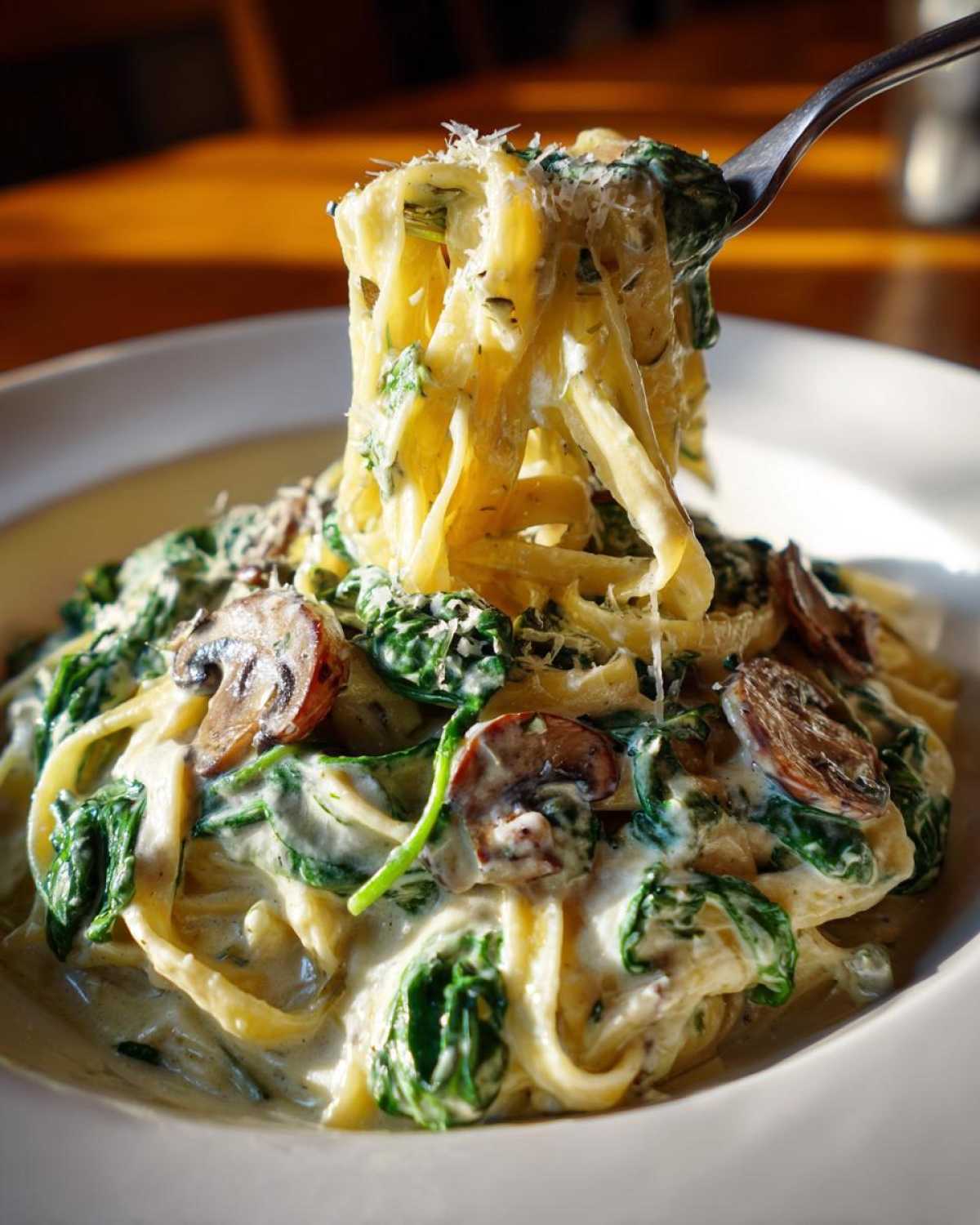 A fork lifting fettuccine noodles coated in creamy sauce, spinach, and mushrooms from a bowl of Creamy Spinach and Mushroom Pasta Dinner.
