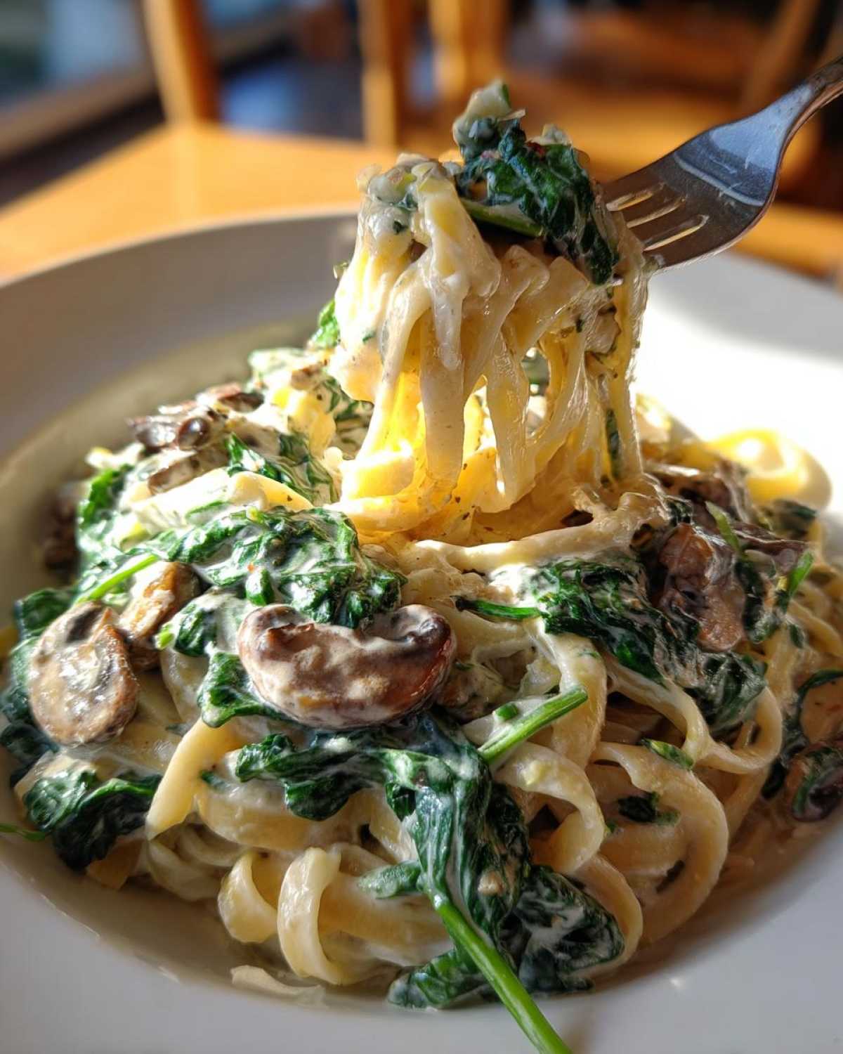 A fork lifting fettuccine coated in a rich sauce with spinach and mushrooms from a bowl of Creamy Spinach and Mushroom Pasta Dinner.