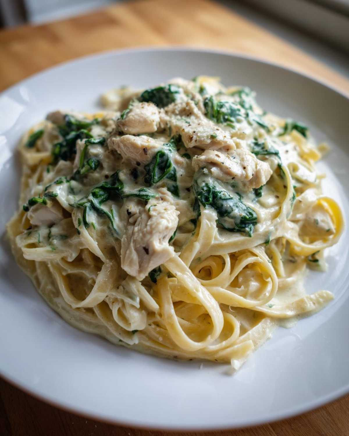 Close-up of Creamy Spinach Chicken Pasta with Garlic featuring fettuccine noodles, chunks of chicken, and wilted spinach in a rich white sauce.