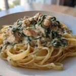 A close-up of a serving of Creamy Spinach Chicken Pasta with Garlic featuring fettuccine noodles and chunks of chicken in a rich sauce.