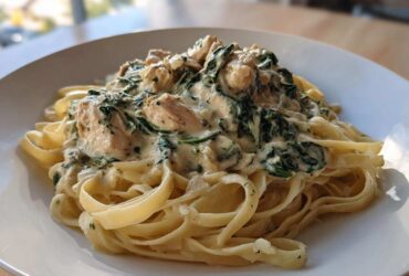 A close-up of a serving of Creamy Spinach Chicken Pasta with Garlic featuring fettuccine noodles and chunks of chicken in a rich sauce.