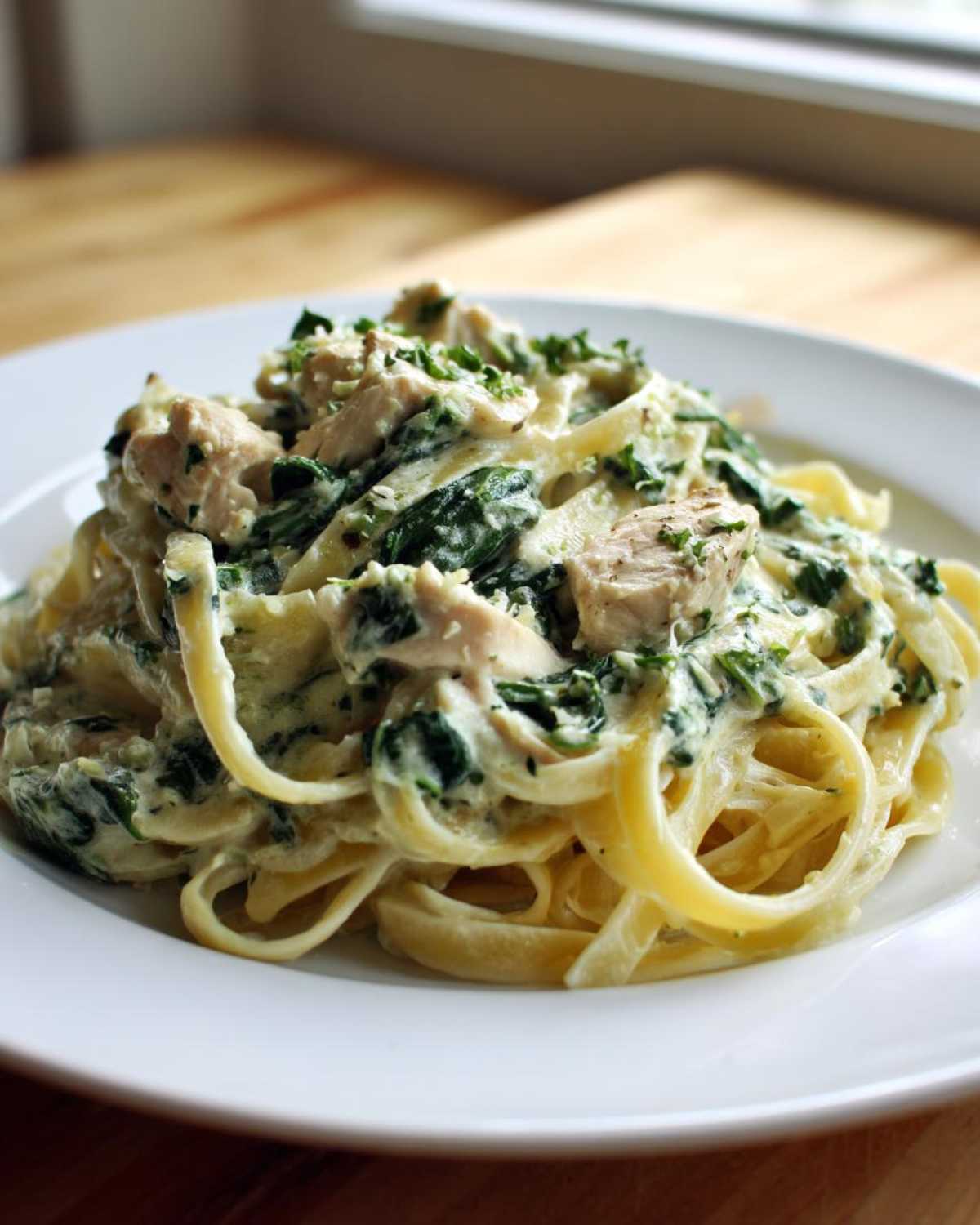 A close-up of creamy spinach chicken pasta featuring fettuccine noodles, chunks of chicken, and fresh parsley garnish.