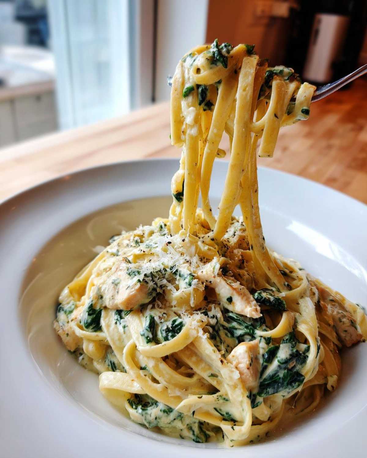 A fork twirls linguine coated in a rich sauce with chicken and spinach from a bowl of Creamy Spinach Chicken Pasta with Garlic.
