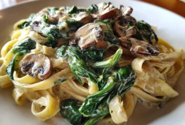 A close-up of fettuccine coated in a rich white sauce, topped with wilted spinach and sliced mushrooms, ready for a Creamy Spinach and Mushroom Pasta Dinner.