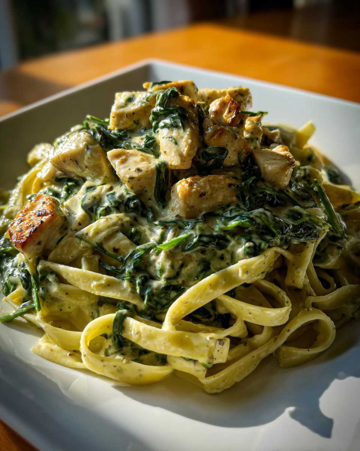 Close-up of fettuccine pasta tossed in a creamy sauce with spinach and topped with seasoned chicken pieces for a Creamy Spinach Pasta with Chicken Dinner.