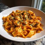 A close-up of a white bowl filled with Creamy Sun Dried Tomato Pasta with Chicken, garnished with fresh herbs.