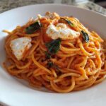 A close-up of a white bowl filled with Creamy Tomato Pasta with Burrata Cheese and fresh basil leaves.
