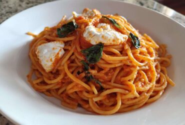 A close-up of a white bowl filled with Creamy Tomato Pasta with Burrata Cheese and fresh basil leaves.