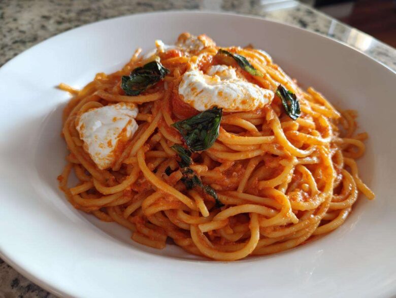 A close-up of a white bowl filled with Creamy Tomato Pasta with Burrata Cheese and fresh basil leaves.