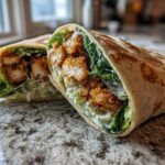 Two halves of a Crispy Chicken Caesar Wrap with Parmesan showing crispy chicken, romaine lettuce, and creamy dressing inside a toasted tortilla.