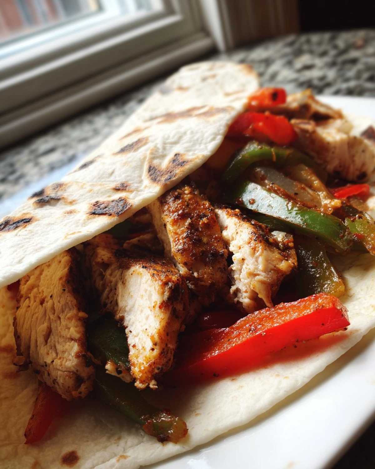 Close-up of seasoned, sliced chicken breast served with sautéed green and red peppers inside a warm tortilla for Crispy Chicken Fajitas.