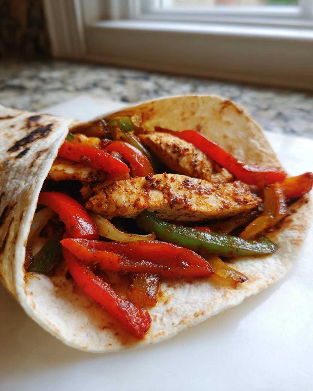 A close-up view of a warm tortilla filled with seasoned chicken strips and sautéed peppers, ready to eat as Crispy Chicken Fajitas.