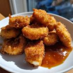 A pile of golden brown, crispy chicken nuggets served with a side of glistening honey garlic dip.