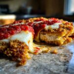 Close-up of Crispy Chicken Parmesan with melty cheese stretching as the piece is pulled apart, topped with rich tomato sauce.