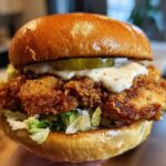 A perfectly assembled Crispy Chicken Sandwich with Garlic Sauce, featuring a thick fried patty, pickles, and lettuce on a brioche bun.
