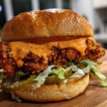 A close-up of a delicious Crispy Chicken Sandwich with Spicy Mayo dripping over the fried chicken fillet, lettuce, and pickles.