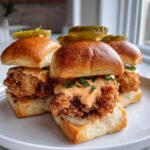 Three Crispy Chicken Sliders with Spicy Mayo piled high on soft buns, topped with pickles.