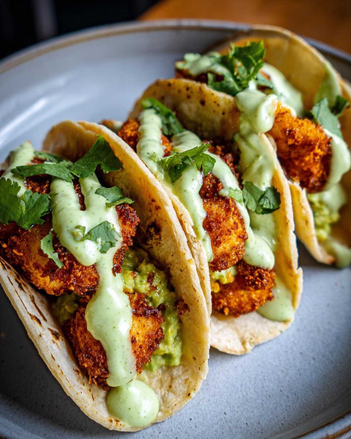 Three Crispy Chicken Tacos loaded with avocado mash and drizzled generously with avocado cream sauce.
