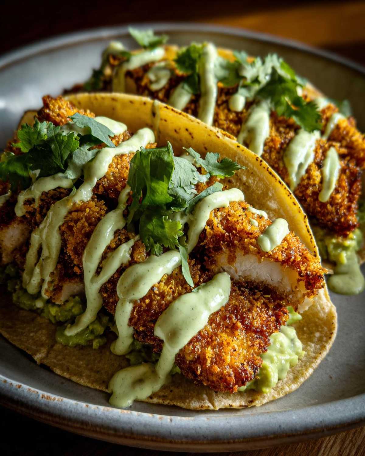 Two Crispy Chicken Tacos topped with bright green avocado cream drizzle and fresh cilantro.