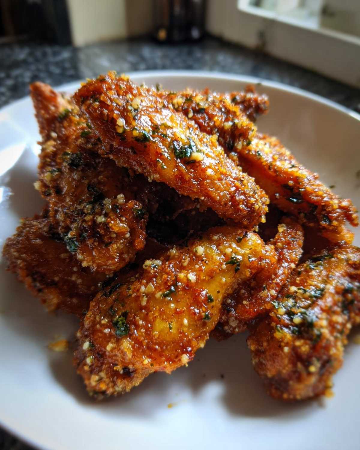 A close-up of golden brown Crispy Chicken Wings with Garlic Parmesan Sauce piled in a white bowl.