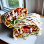 Cross-section of a Crispy Chicken Wrap with Creamy Garlic Sauce drizzled over fresh lettuce, tomato, and crispy chicken.